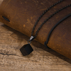 Cube Black necklace arranged on a leather notebook and timber