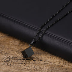 Cube Black necklace laid on a black leather surface