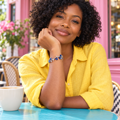 Eden in Cobalt with a silver-tone finish, worn with a yellow shirt at a colourful café.
